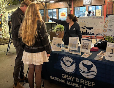 People standing by a table with information about whales. The table reads Gray's Reef National Marine Sanctuary and has NOAA and ONMS logos