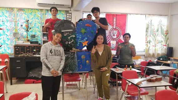 Students in a classroom pose next to their marine debris sculptures. 