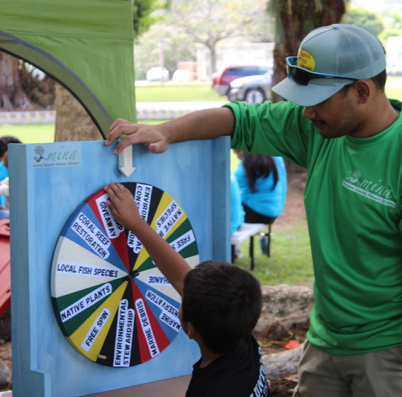A volunteer at a community event plays a spin wheel educational game with a child. 