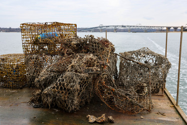 A pile of broken crab traps covered in algae sit on the back of a boat on a cloudy day.