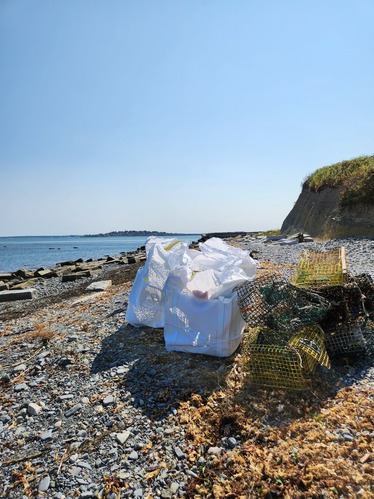 Derelict fishing gear placed next to two full white trash bags on a rocky shoreline.