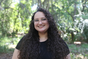 A person smiling with trees in the background.