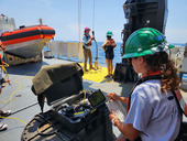 People in protective gear on a ship looking at a monitor