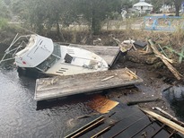 A derelict vessel and other debris pushed along a shoreline.