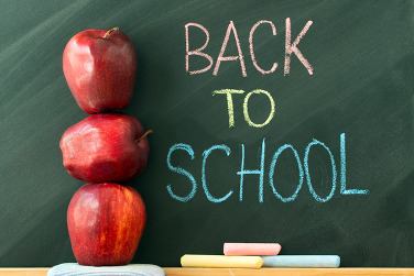 Three red apples stacked on top of each other next to a chalk board with “Back to School” written on it.