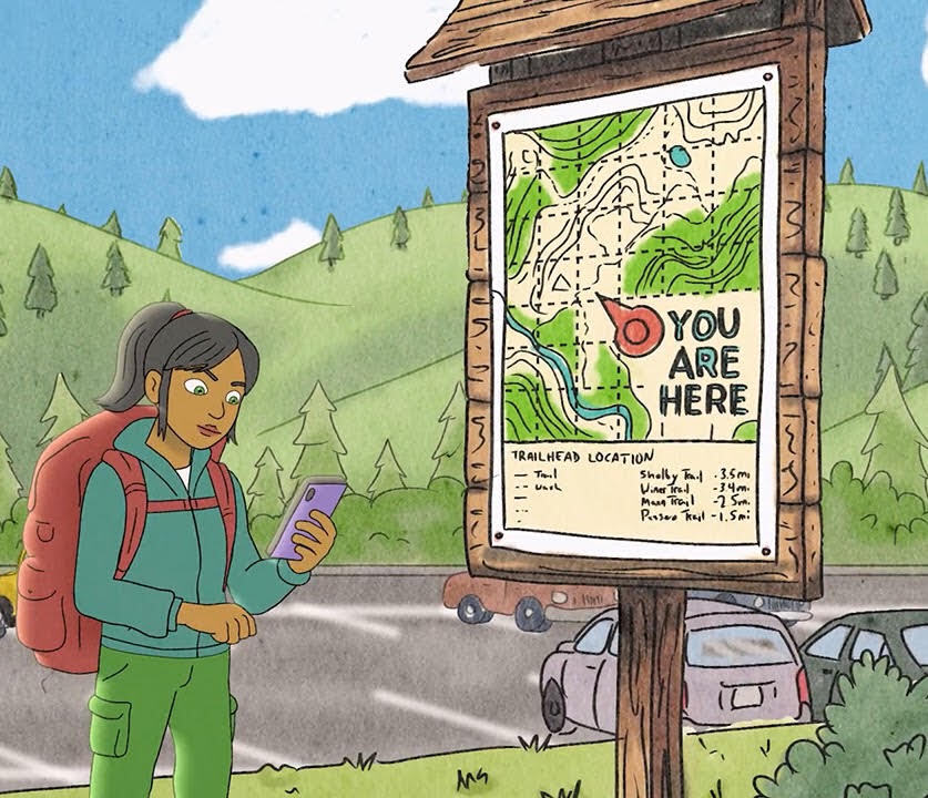 A hiker checks her phone beside a trail kiosk map marked "You Are Here" in a scenic mountain area.