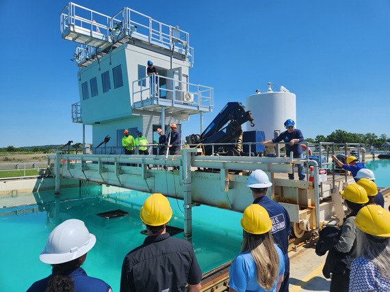 Workshop participants wearing hardhats gather around a large tank of water at an oil spill response and research test tank.