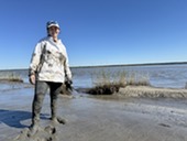 Person standing in a Georgia salt marsh, smiling in a mud flat. 