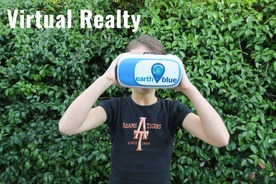 A young girl in an Adams Tiger T-shirt holding virtual reality goggles with an Earth is Blue sticker to her eyes.