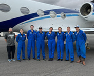 A group of people in blue flight suits standing in front of an airplane