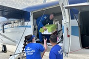 A pilot in a flightsuit standing aboard an aircraft receives a box from a SeaWorld employee