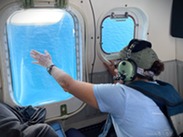 An observer looks out the window of a NOAA Twin Otter aircraft