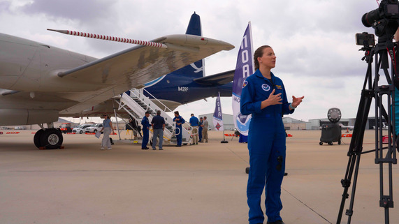 A NOAA Hurricane Hunter crew member gives a media interview with a NOAA WP-3D Orion aircraft in the background