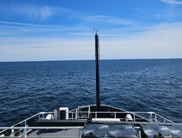 view from the bridge of a ship, overlooking a white bow with blue sky and sea 