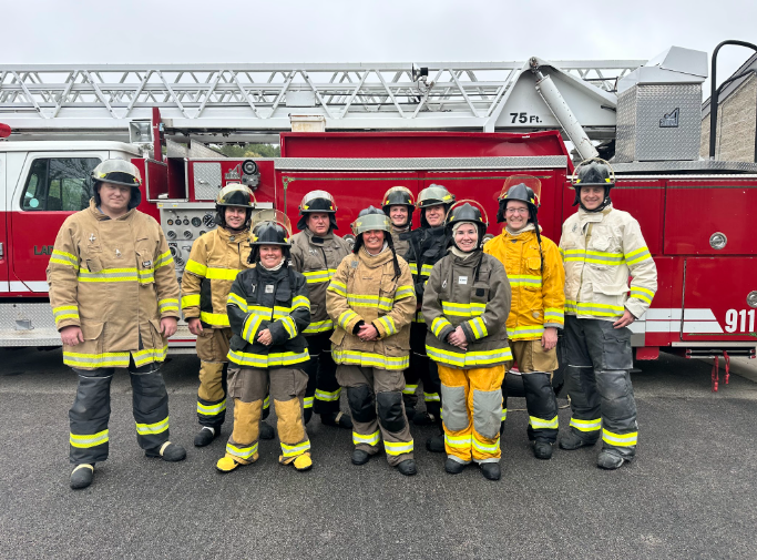 Individuals standing in front of a firetruck in turn out gear 