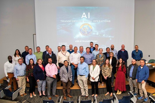 Representatives of the AI task forces pose in front of a slide reading "AI Transforming Naval Operations"