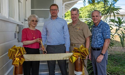 President Ann Rondeau holds a giant scissors and stands with three other leaders behind a gold ribbon.