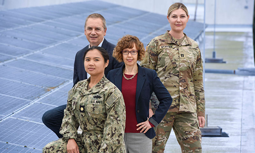 Two faculty members and two military students in uniform stand in front of solar panels.