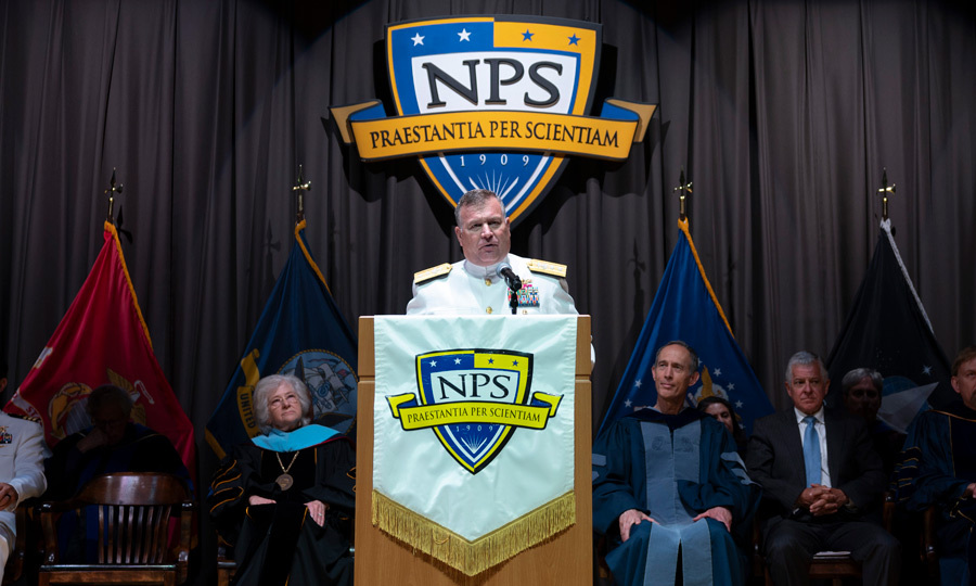 man in a white naval uniform at a podium with NPS logo