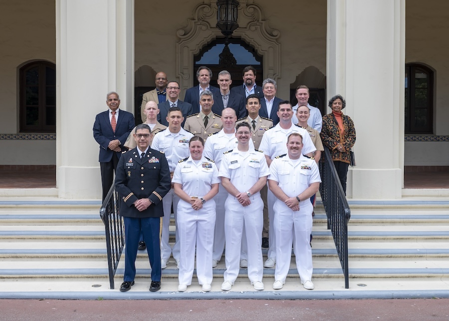 Men and women in uniforms and suits standing on the steps of a building, flanked by white pillars