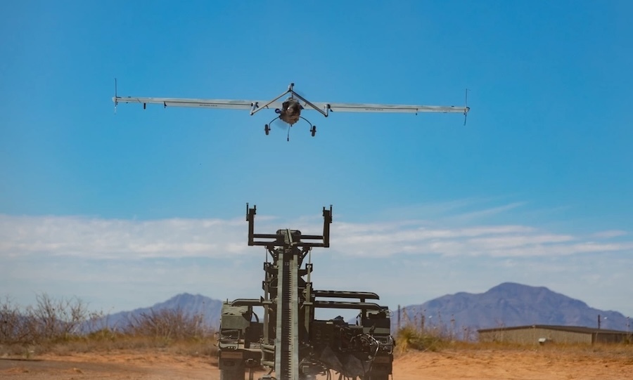 green launch seen from the front with a just-launch plane overhead, blue sky and desert mountains in background