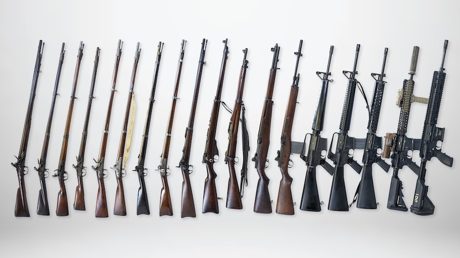18 rifles of various ages lined up vertically on a white background