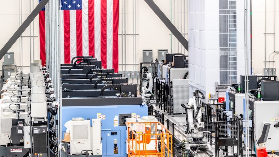 machinery on factory floor in foreground with a large american flag hanging on back wall