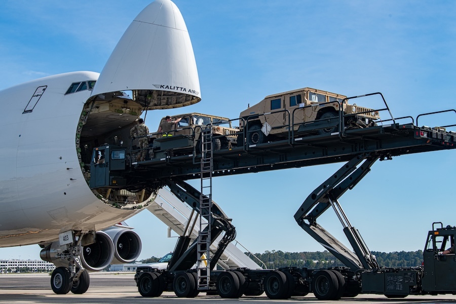 front of airplane with an open nose cone; an elevated truck bed raising two Humbvees to the height of the plane's nose