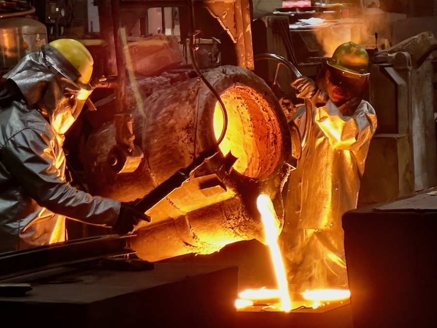 two people in protective gear pour glowing molten metal 