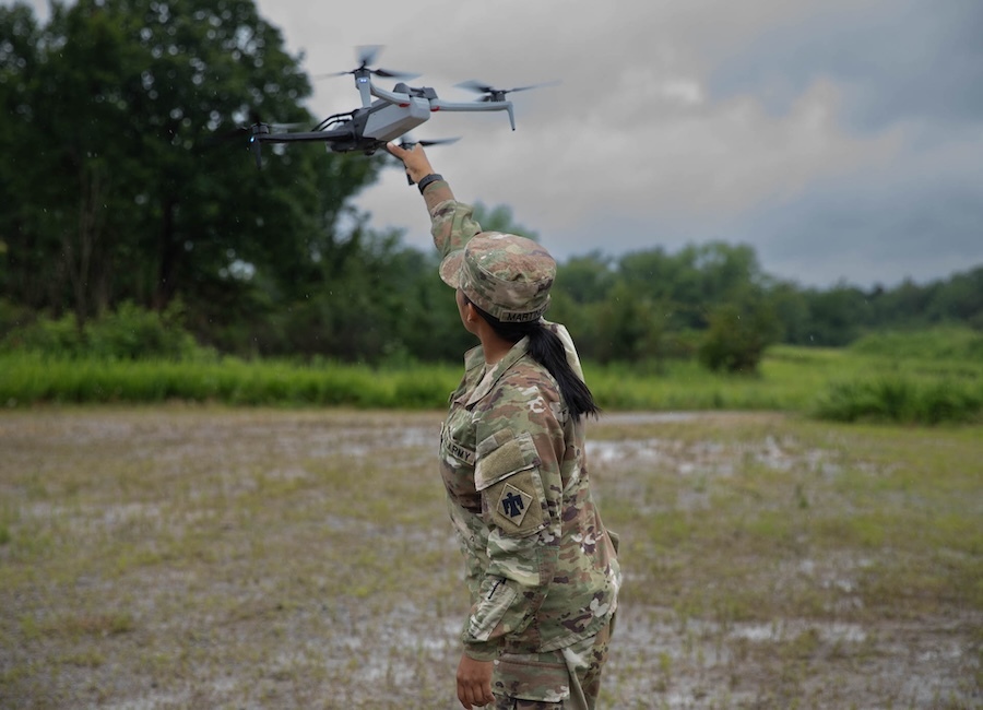 woman fatigues, back to camera, holding a drone aloft