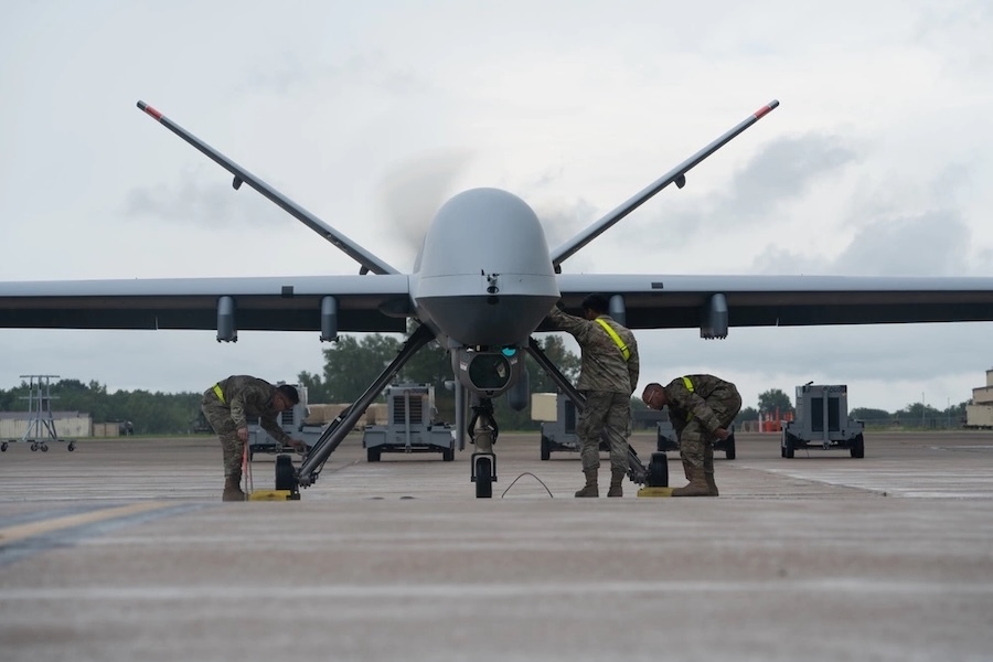 three airmen working under the wings of a around a reaper drone
