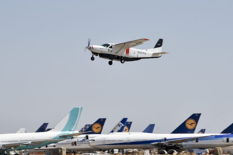 small plane in flight over planes parked below