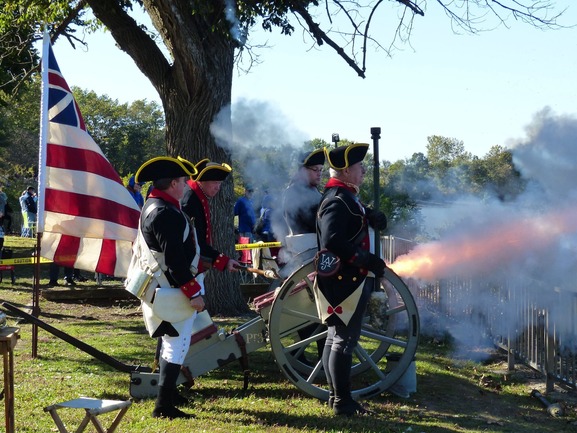 men in revolutionary war uniforms fire a cannon on wheels