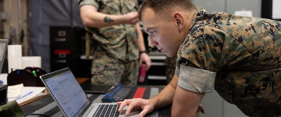 marine in camo bent over an open laptop