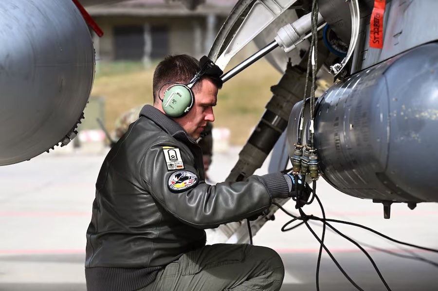 airman in ear protectors crouched next to a plane