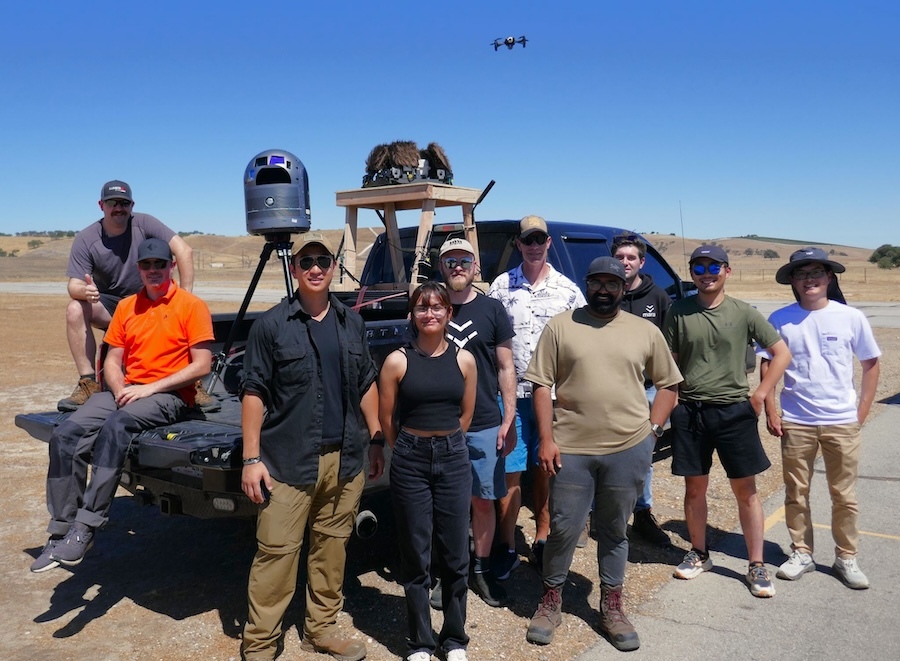 people pose in front of a black pickup truck loaded with technical gear
