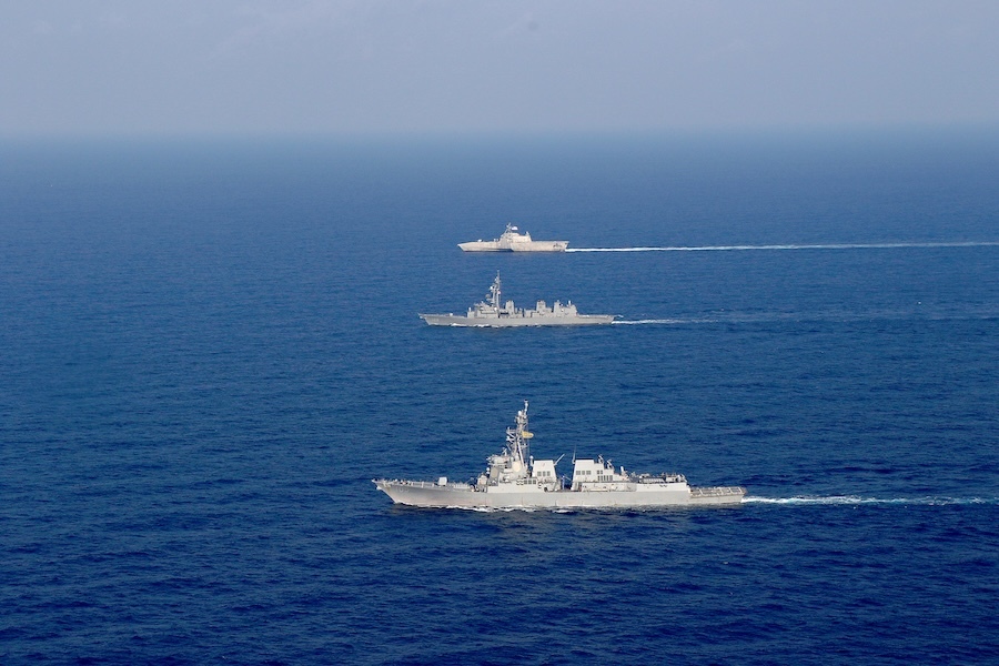 two destroyers and a combat ship crossing a calm, blue sea