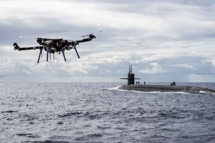 drone flying over water toward a surfaced submarine