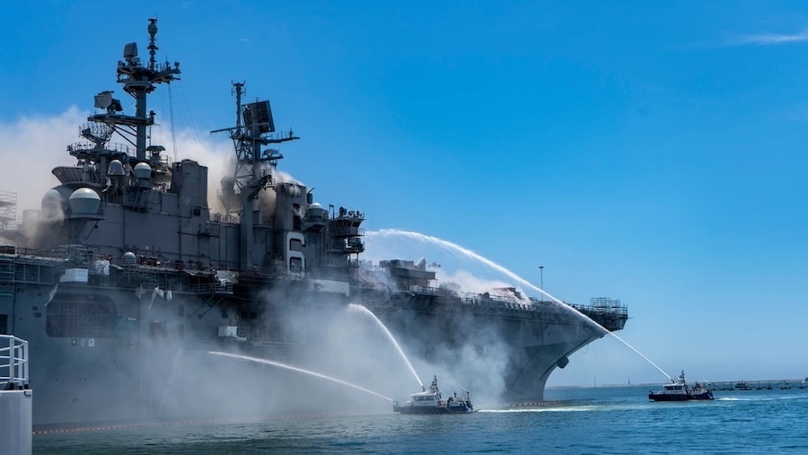 two small boats spraying water on a large burn ship
