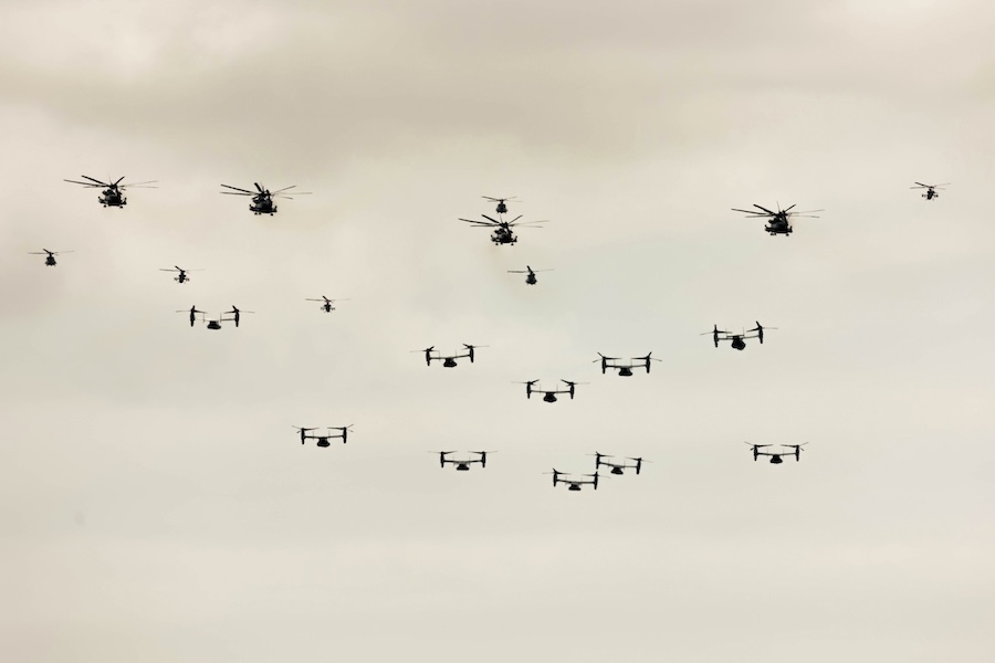 Swarm of drones in flight, silhouetted against a white sky