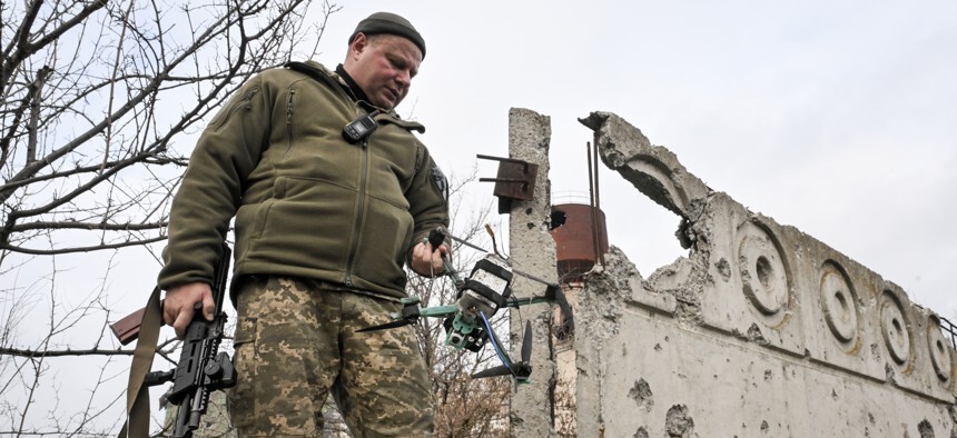 man in fatigues holds a rifle in one hand and a drone in the other