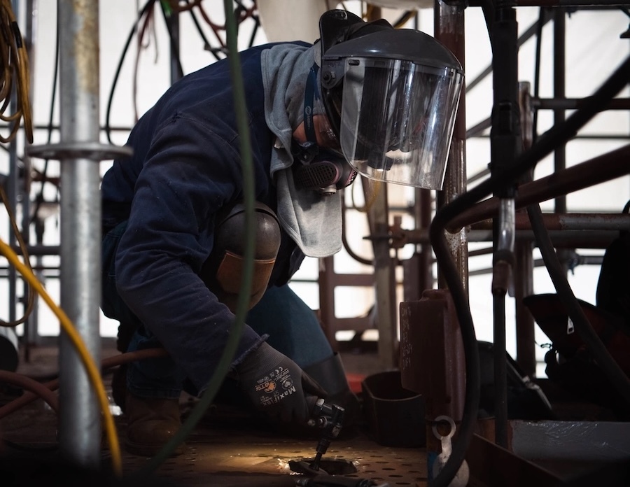 worker in protective gears kneels with a tool