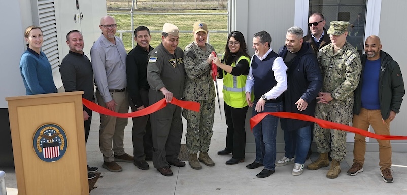 group of people standing behind a newly-cut red ribbon, center two holding giant scissors