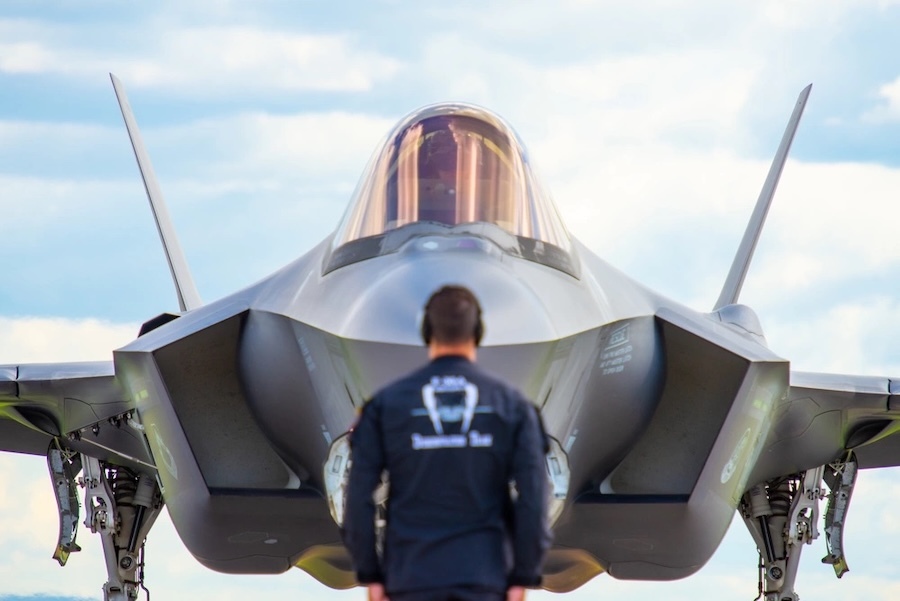 fighter jet facing the camera with a man in blue standing directly in front of it