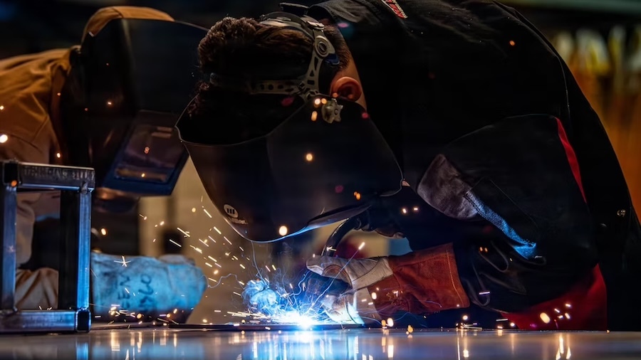 two welders in helmets bent over a torch