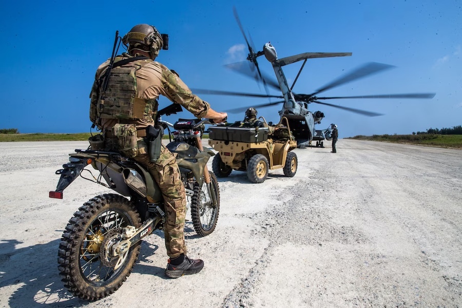 man on a motorcycle lined up behind a tactical vehicle waiting to load a helicopter