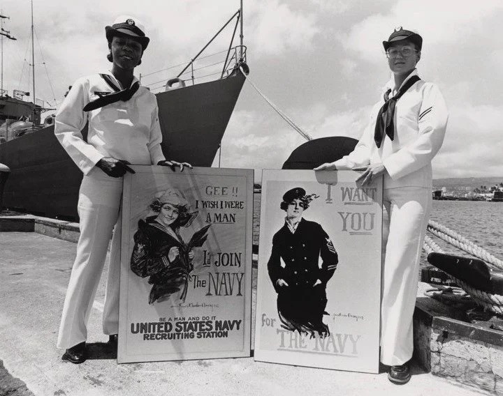 two women in navy uniforms standing beside recruitment signs