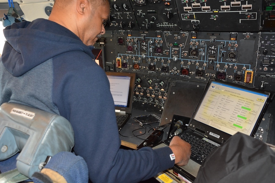 man in front of a complex control panel uses two laptops