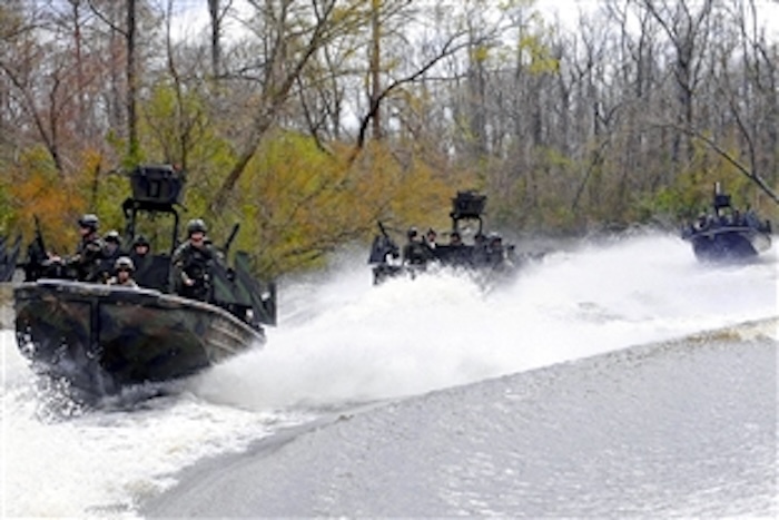 three motorboats proceed along a river, throwing up spray.jpg