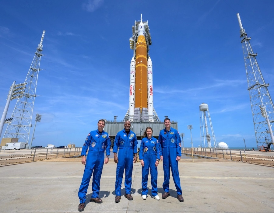 astronauts pose in front of a rocket